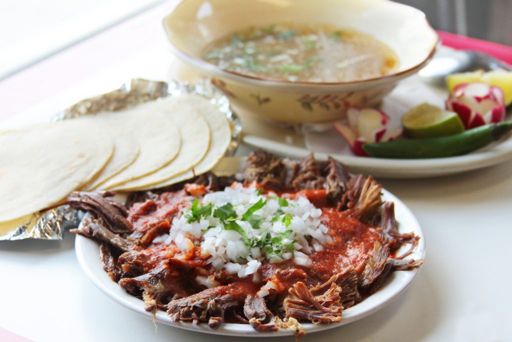 Mexican meat in a specialty Mexican dish with tortillas and sopa in the background