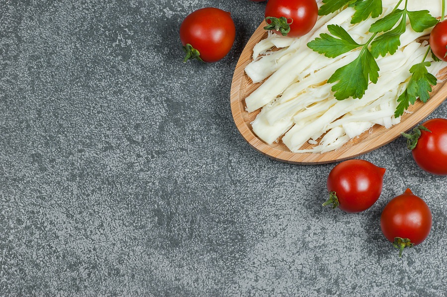 White asadero cheese with tomatoes and greens on cutting board.