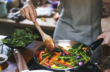 Chef cooks meat and vegetables on pan with freshly cut cilantro on the side. 