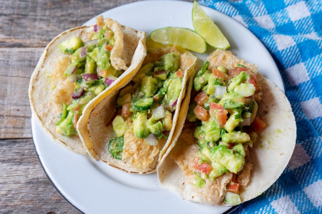 chicharron tacos on a white plate with some avocado and salsa