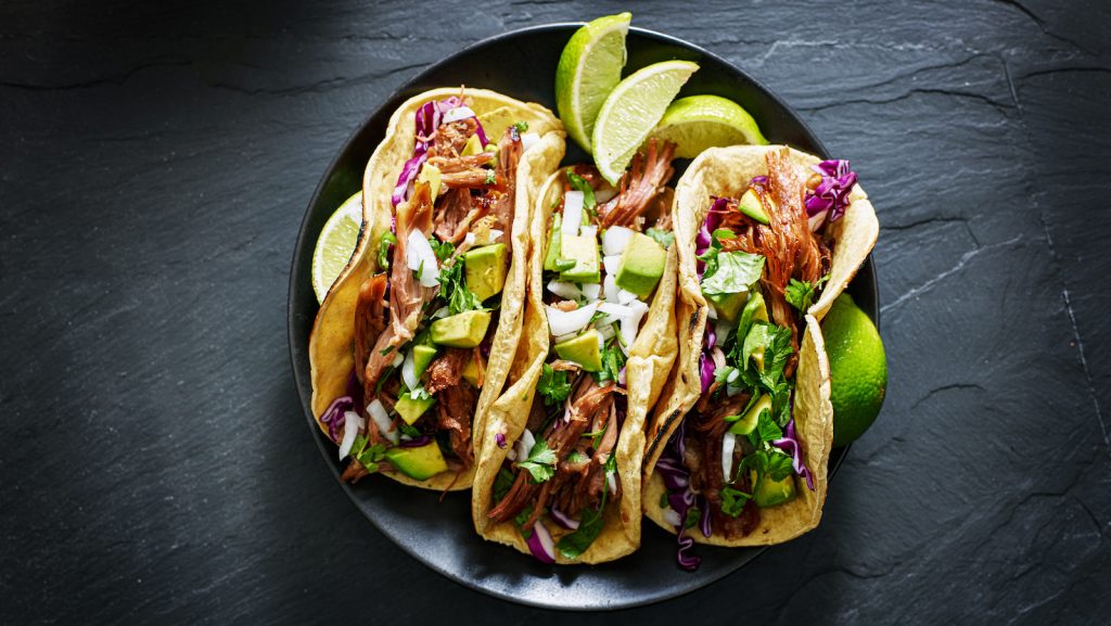 mexican street tacos flat lay composition with pork carnitas, avocado, onion, cilantro, and red cabbage