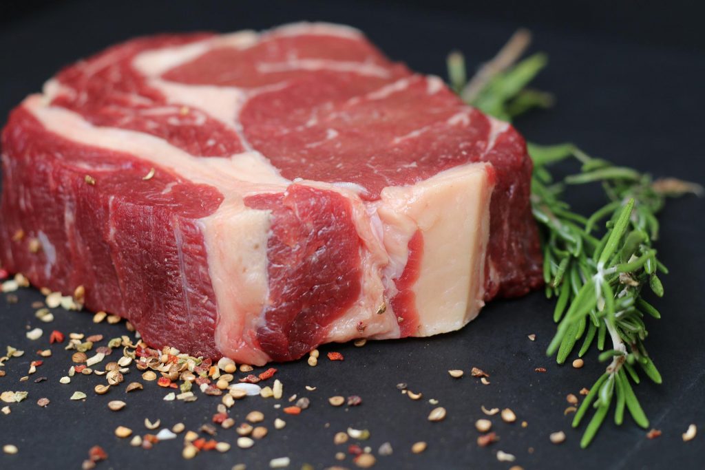 A piece of raw meat atop a black board with seasoning and thyme.